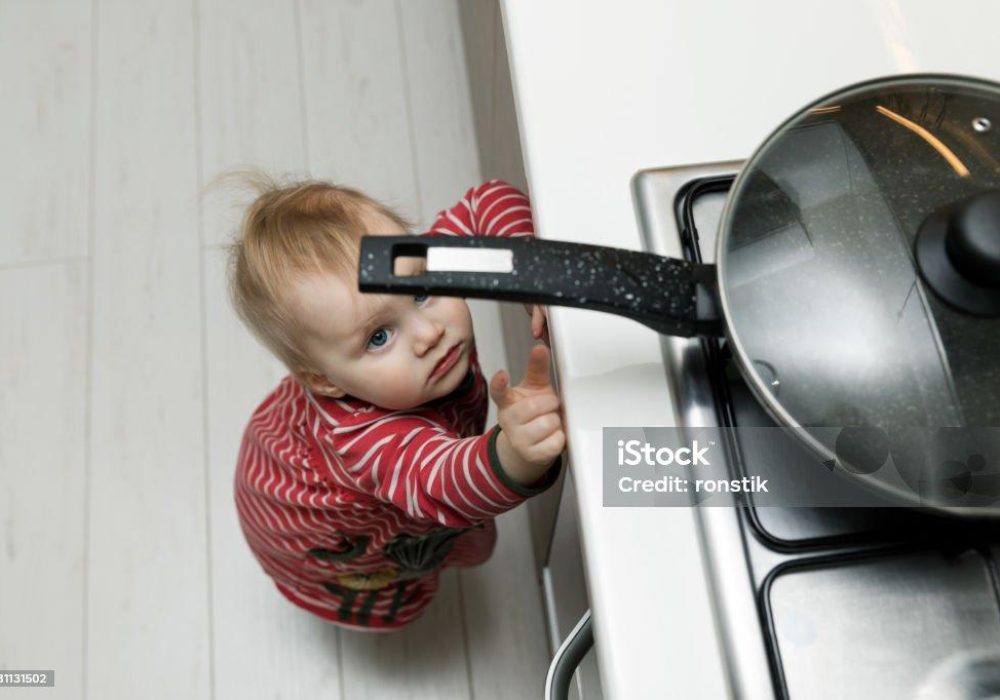 child safety at home concept - toddler reaching for pan on the stove in kitchen
